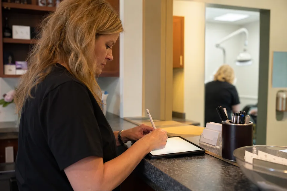 A clinic practice manager signing a proposal on a tablet at the reception counter