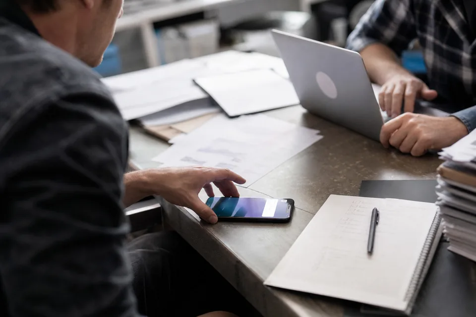 A phone lighting up with a notification beside a printed proposal on an agency desk