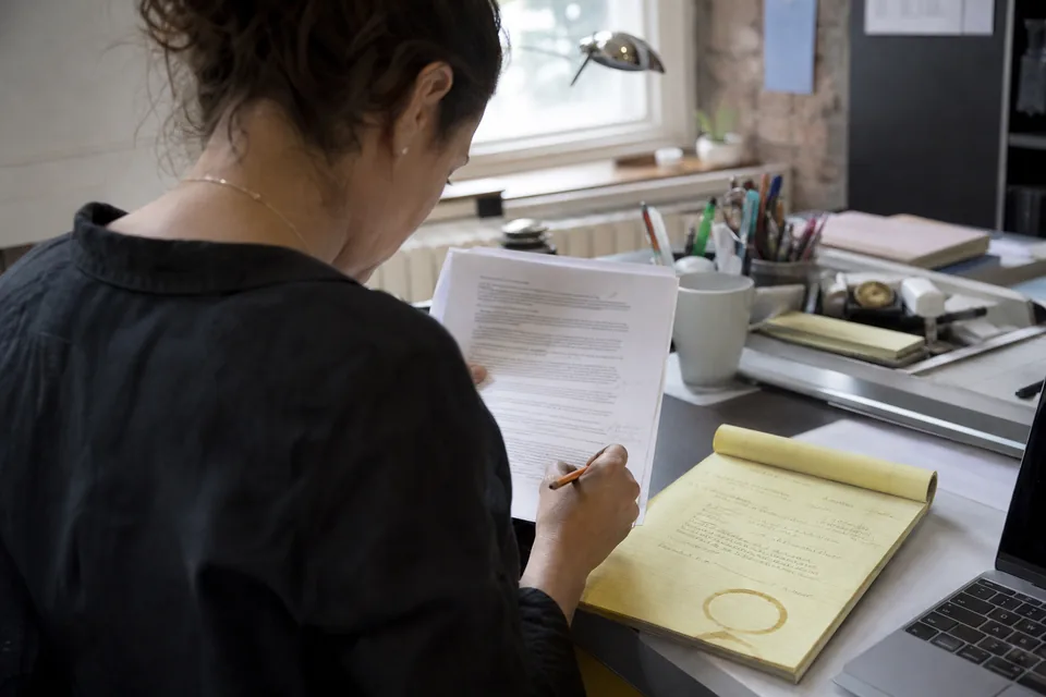 A consultant marking up a freshly printed proposal draft next to her handwritten call notes