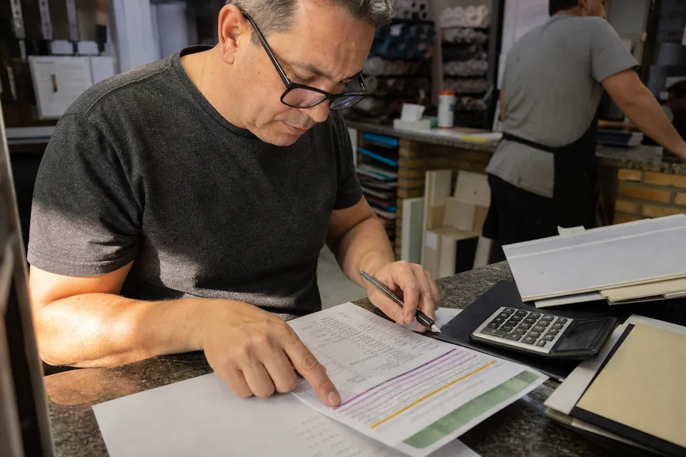 A print shop owner checking line items on a quote against his printed price list