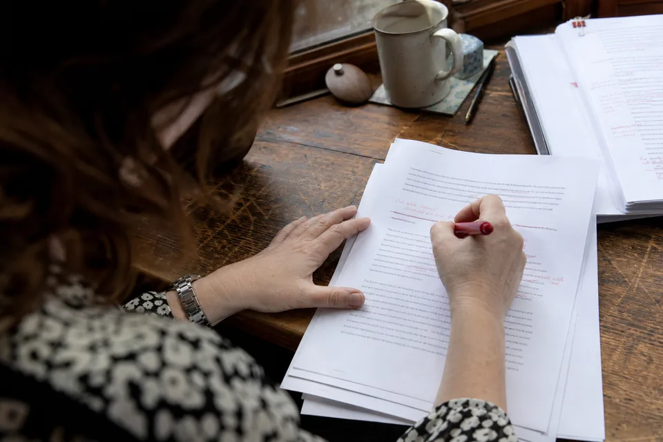 A writer shortening a sentence in a printed executive summary with a red pen